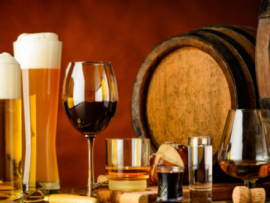alcoholic drinks on wooden table in glasses, mugs and shots with barrel in background
