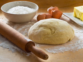 Dough on wooden board with rolling pin.