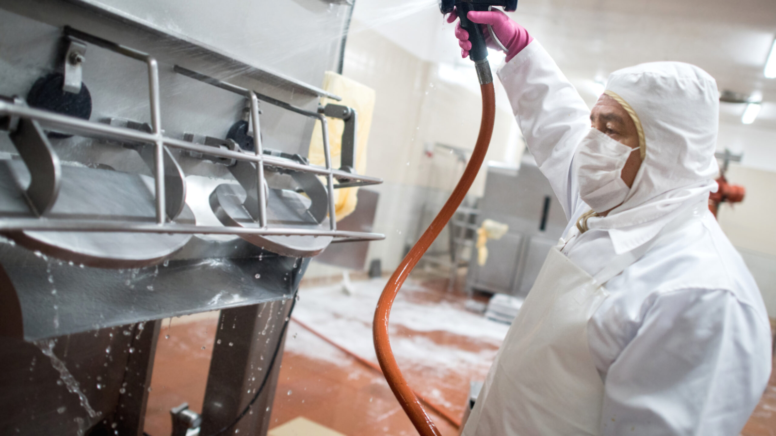 Man washing machines at a factory with a hose